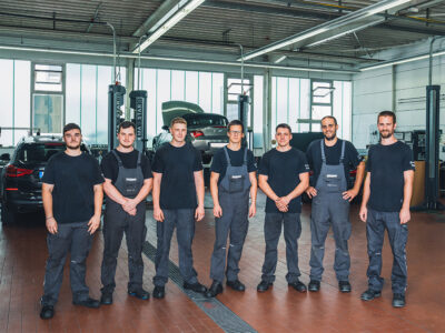 Teamfoto der Kfz-Mechatroniker bei BMW Tschirley in einer modernen Werkstatt mit Premium-Fahrzeugen